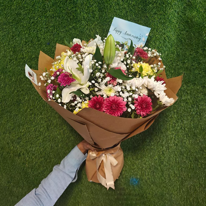 Mixed celebration bouquet with a white Oriental lily, roses, and chrysanthemums in brown Kraft wrap