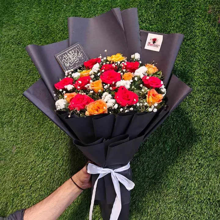 Happy Birthday bouquet featuring red and orange roses and white fillers in modern black wrapping