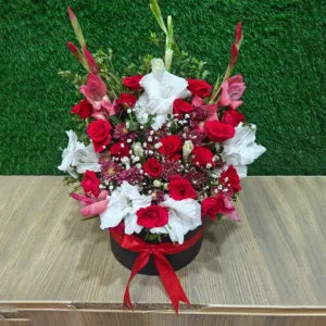 Grand arrangement of red and white flowers, including roses and Gladiolus, in a black round box