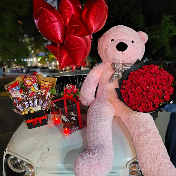 Extreme gift package with large pink teddy bear, 100 red roses bouquet, chocolates, and helium balloons